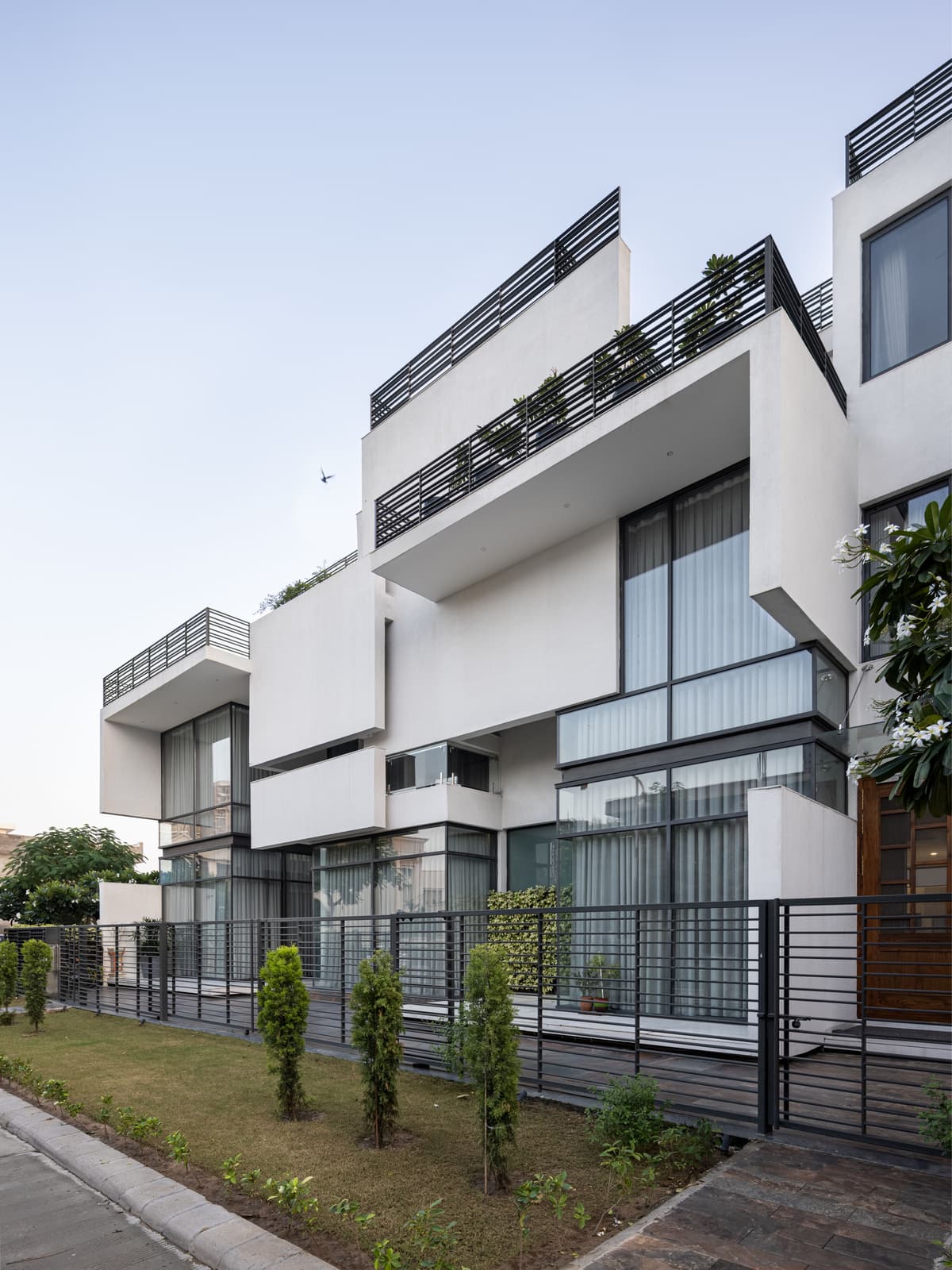 Contemporary façade with interlocking volumes, cantilevered balconies, and extensive glazing; defined by sharp geometry, clean lines, and horizontal black metal railings.