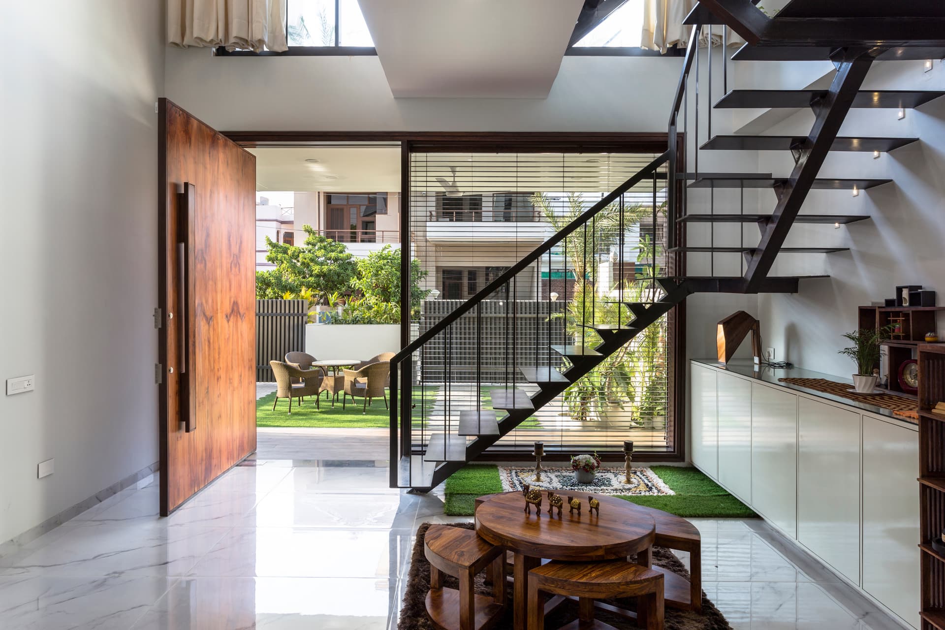 Double-height entry with sleek staircase, wooden accents, and garden views, creating a bright, airy connection between interior and exterior living.