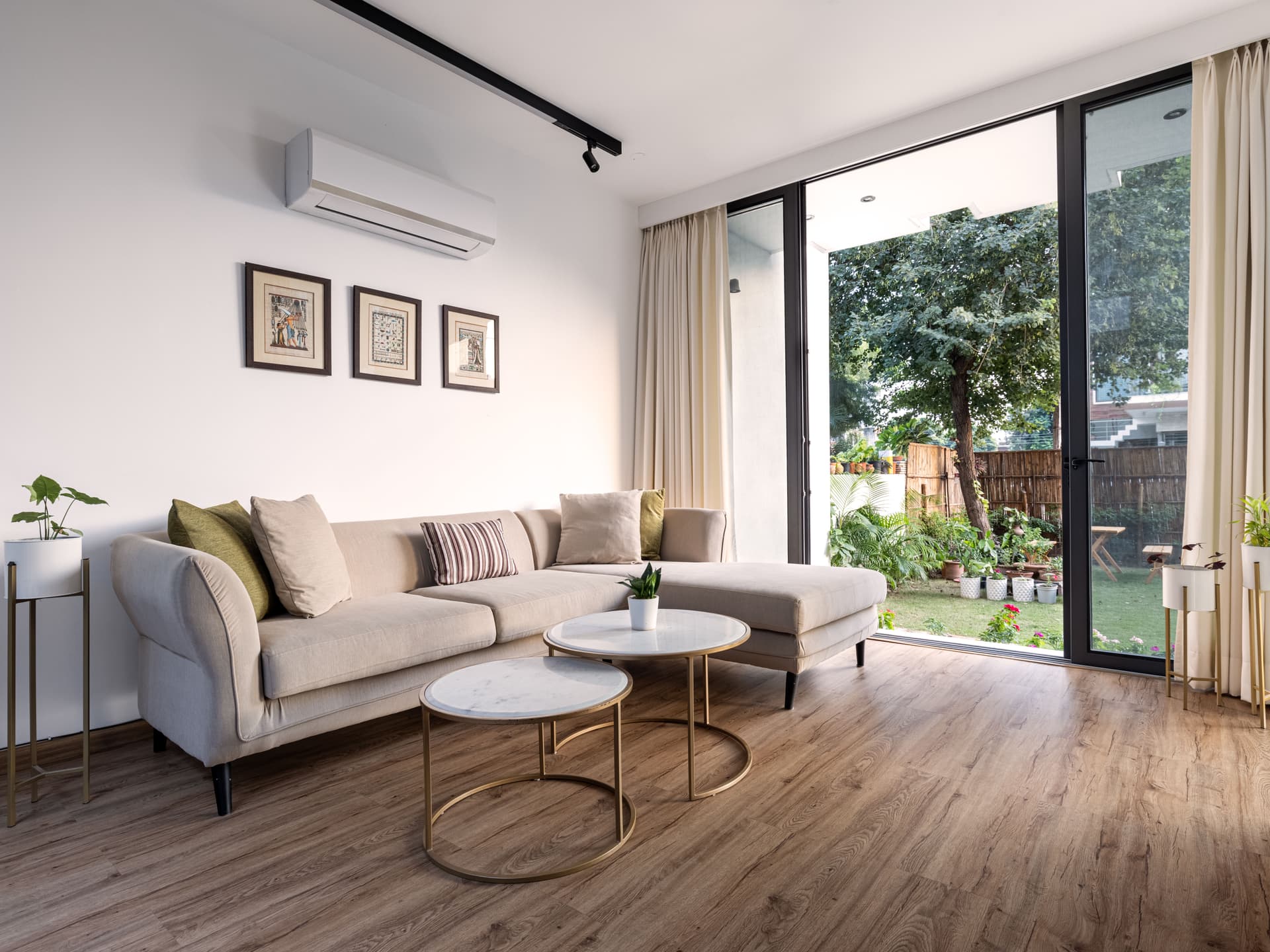 Minimalist living space with large sectional sofa, framed artwork, floor-to-ceiling windows, and direct garden access for abundant daylight and greenery.