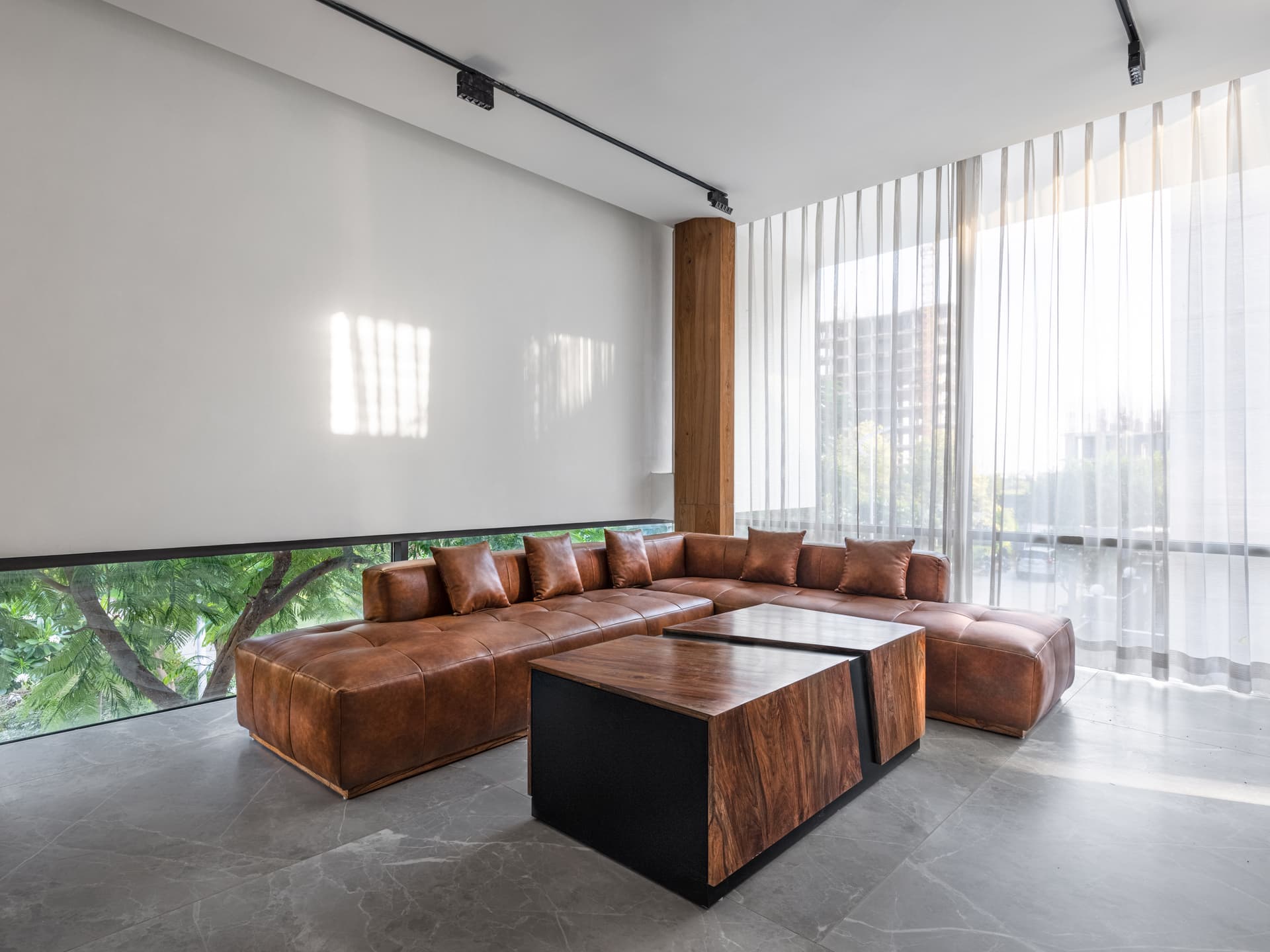 Minimalist lounge with low horizontal glazing, leather sectional seating, sheer drapery, and monolithic furniture composition enhancing spatial clarity and warmth.