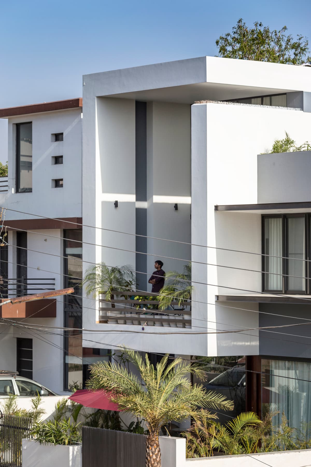 Minimalist balcony with lush plants framed in bold white geometry, offering serene street views and blending privacy with openness beautifully.