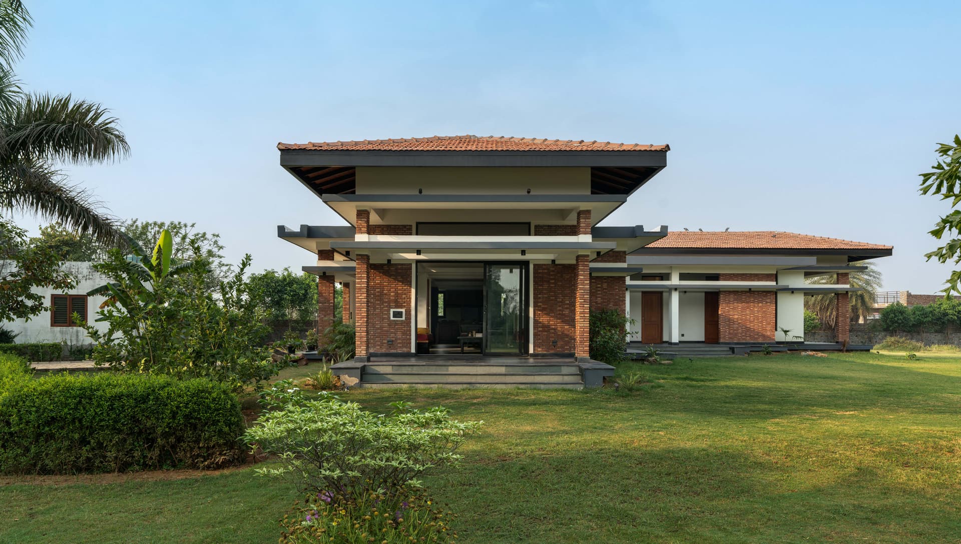 A vaulted wooden roof brings warmth and volume to this living space, creating a striking contrast against the clean white geometry of the walls. Exposed beams emphasize the structural honesty, while the pitched form draws the eye upward, enhancing the sense of openness and connection to nature beyond the sliding doors.