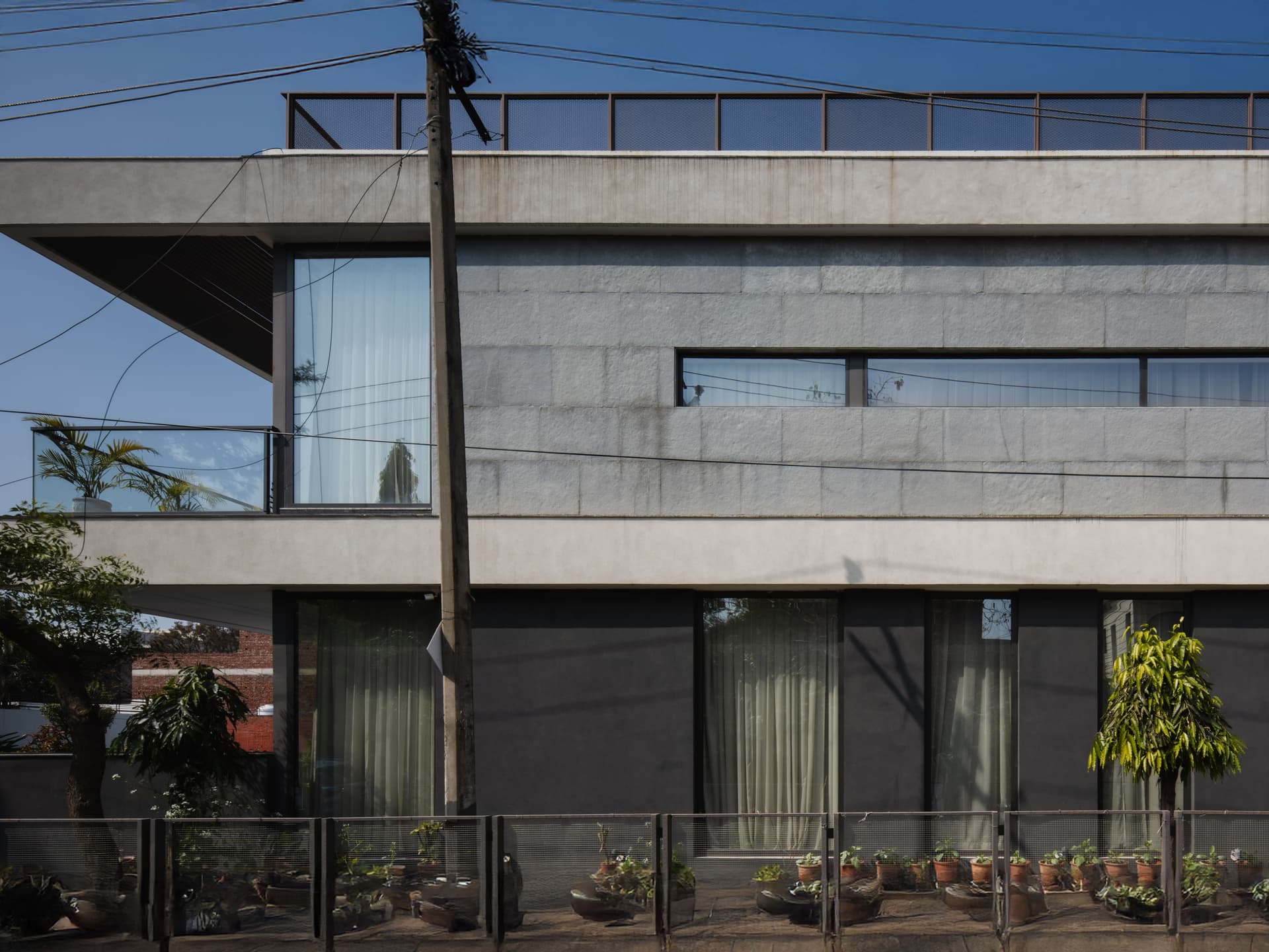 Linear façade composition with horizontal slit windows, stone cladding, and cantilevered balconies emphasize minimalism, privacy, and sharp geometric articulation.