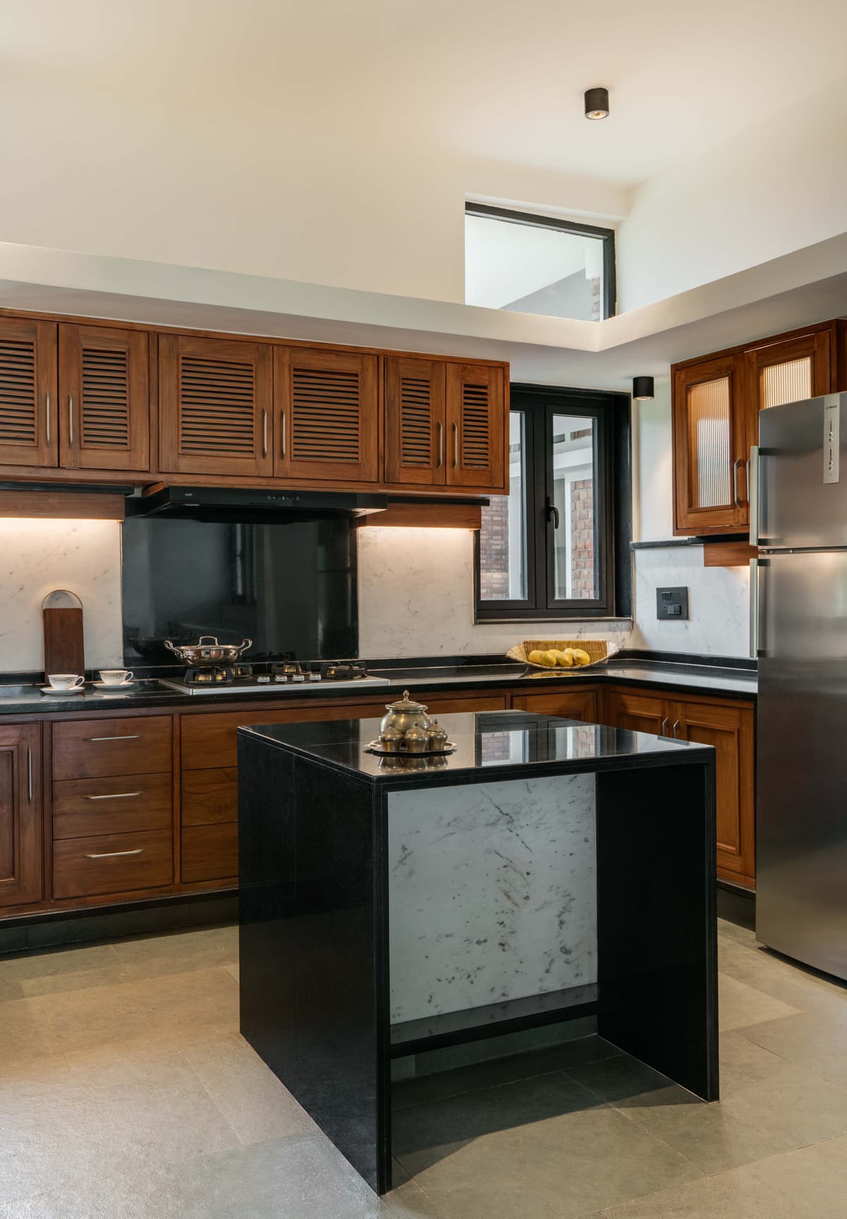 Natural teakwood cabinetry adds an earthy richness, balanced by sleek black granite and subtle marble finishes.