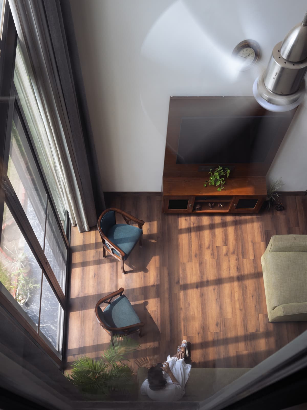 Double-height living space with wooden flooring, large glazing, modern ceiling fan, and minimalist furniture layout enhancing spatial openness and natural light.
