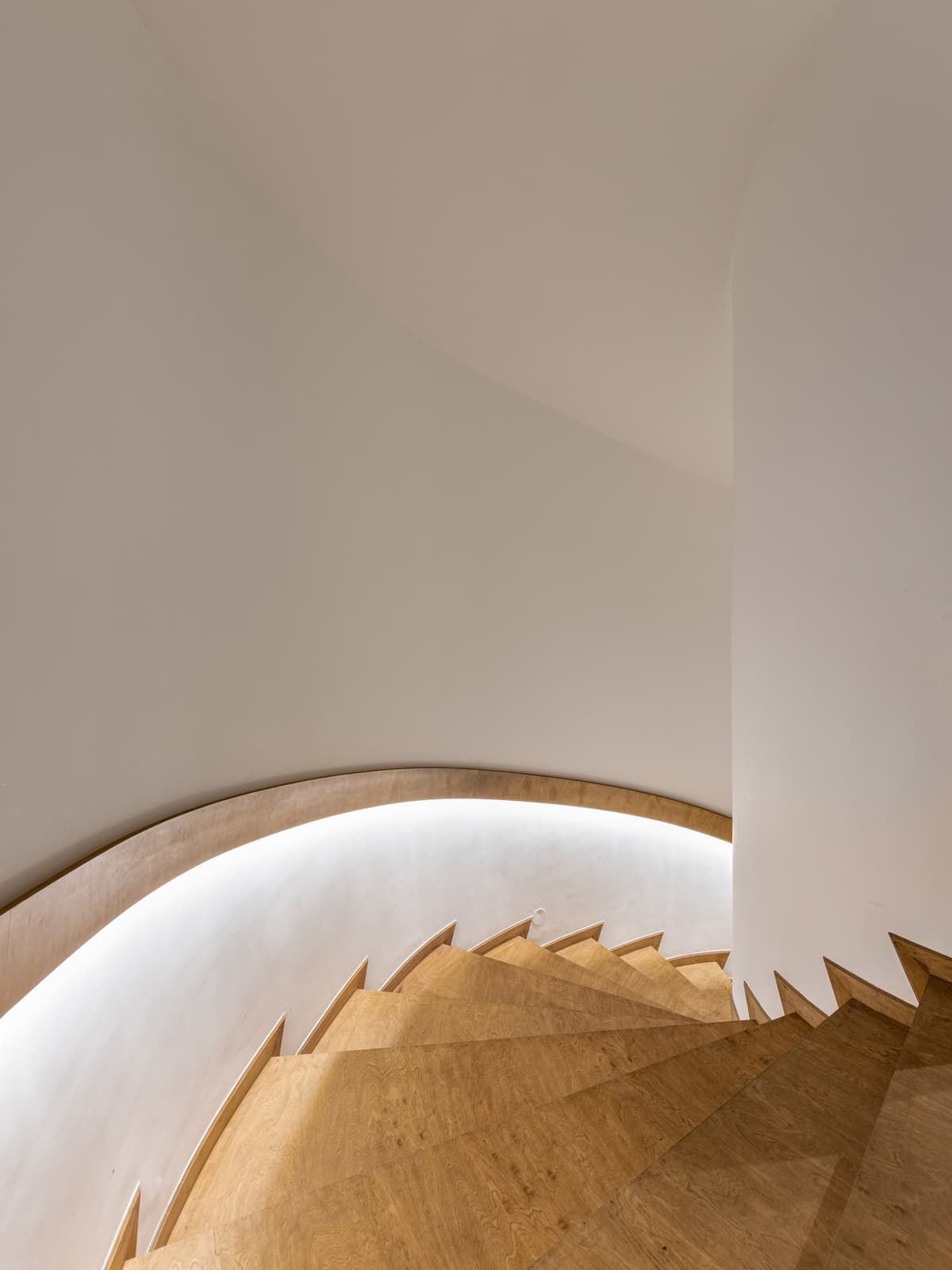 Elegant curved staircase in warm wood finish, integrated LED wall lighting, and continuous flowing form enhancing vertical circulation with sculptural quality.