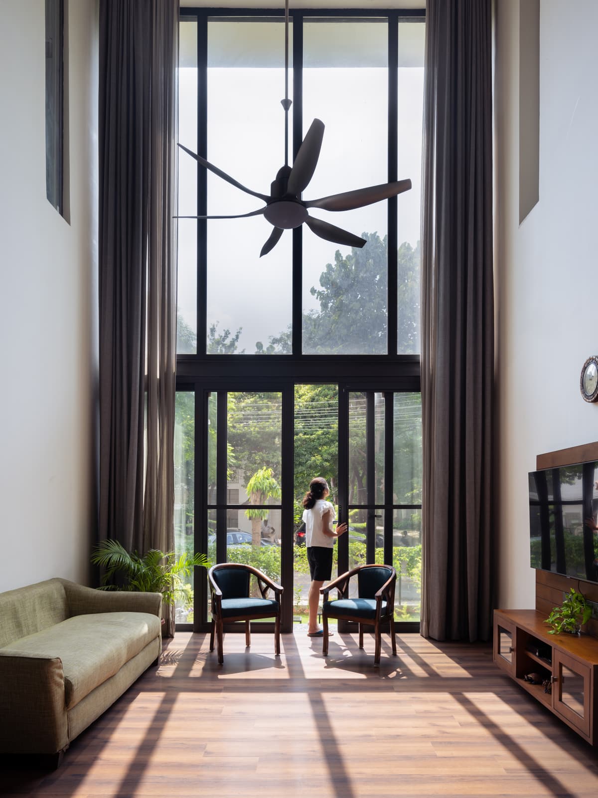 Expansive floor-to-ceiling windows illuminate the voluminous living room; interior features clean lines, wood accents, and modern, minimalist furnishings.