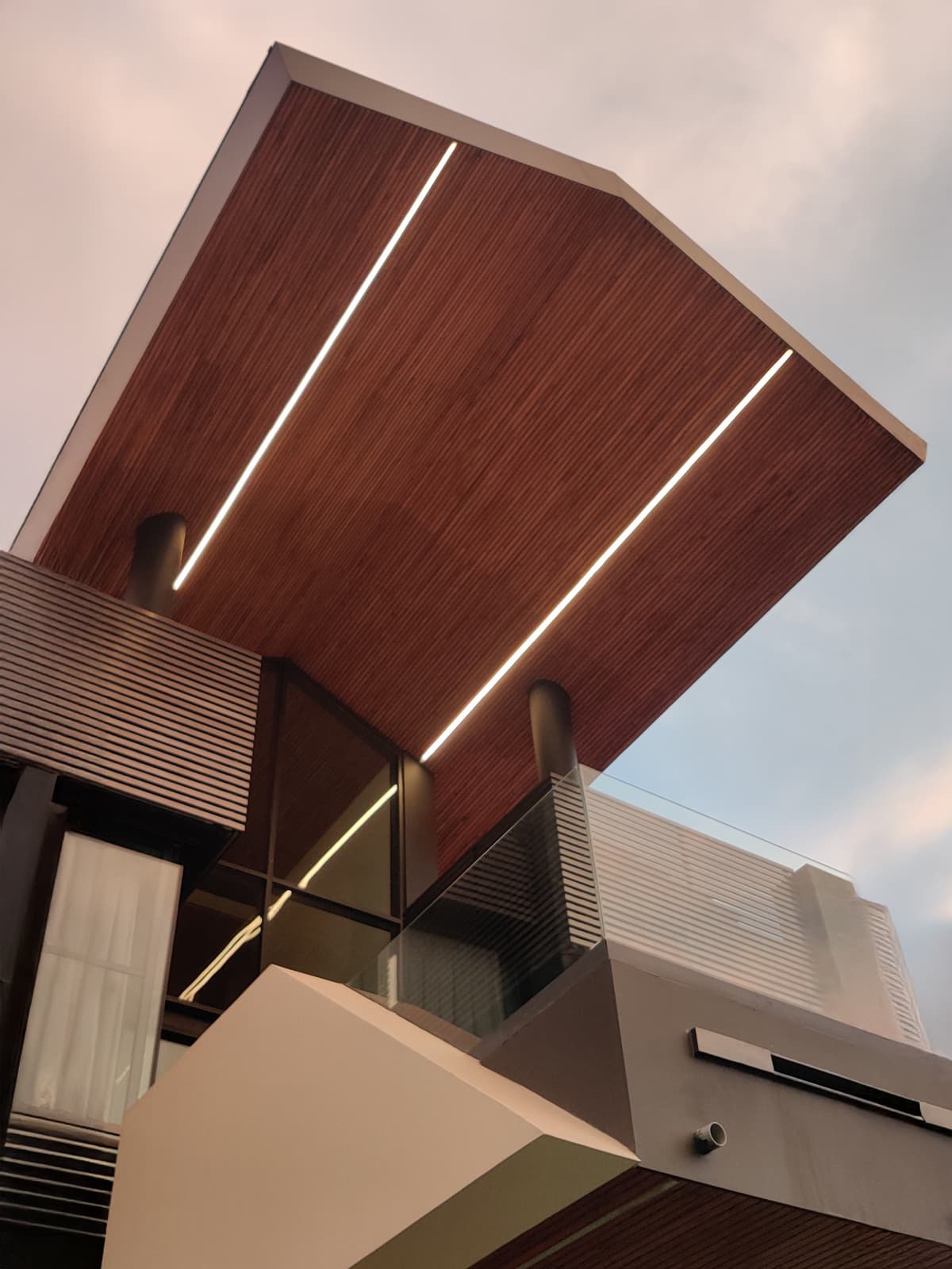 Sloping timber ceiling with recessed lighting, framed by sharp modern edges, adds warmth and dynamic geometry to the bold façade.