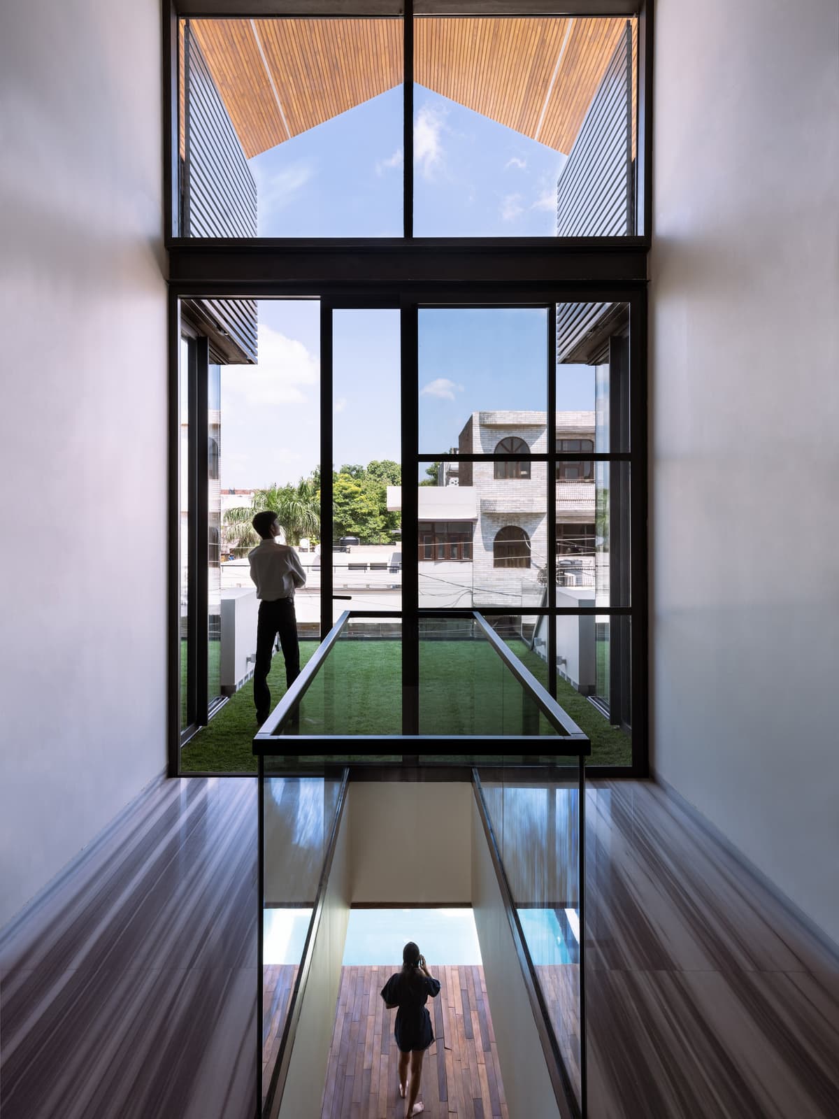 Double-height volume with clerestory glazing, cantilevered grass balcony, and glass bridge enhances light, openness, and vertical spatial connectivity.