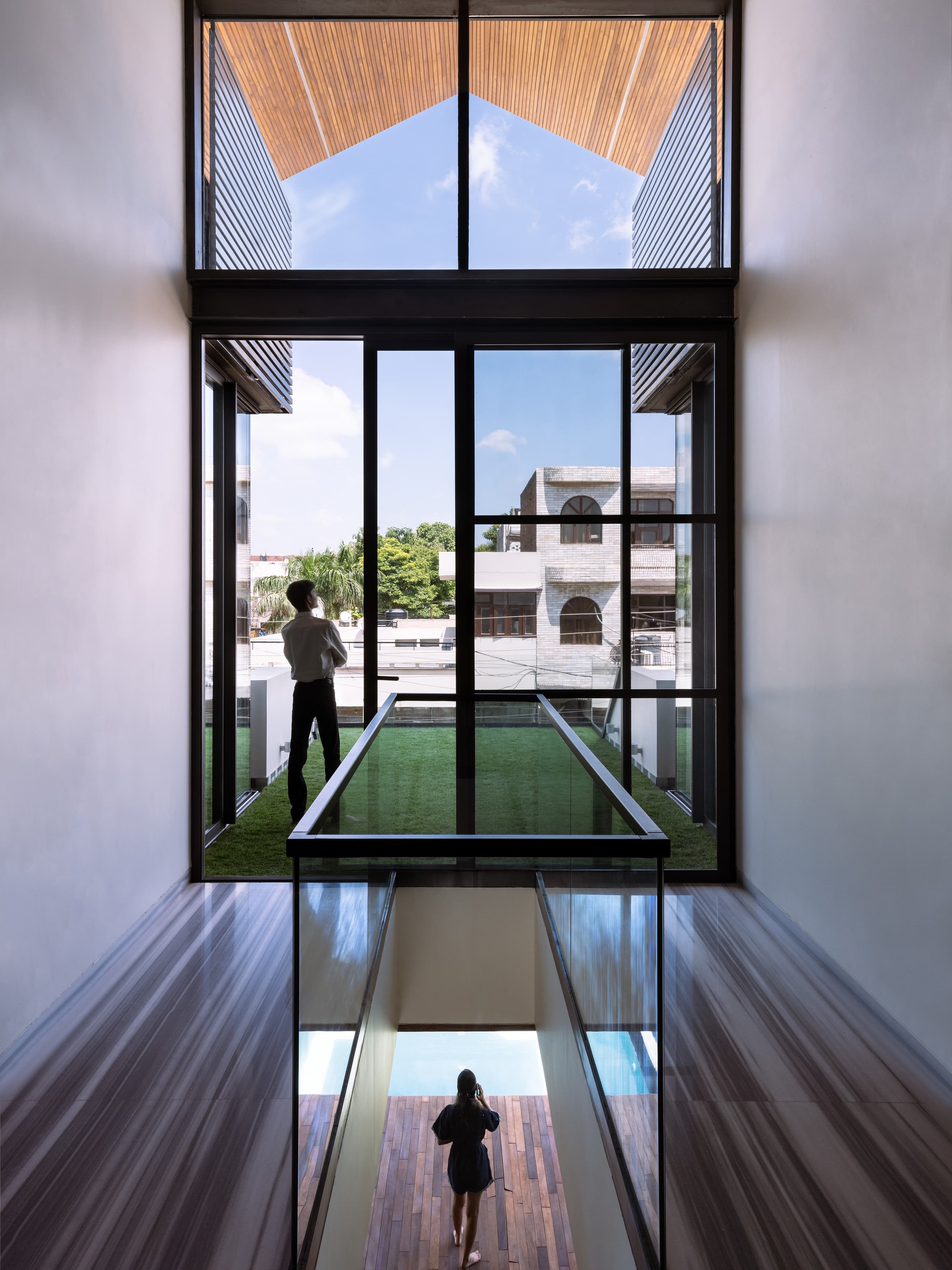 Double-height volume with clerestory glazing, cantilevered grass balcony, and glass bridge enhances light, openness, and vertical spatial connectivity.
