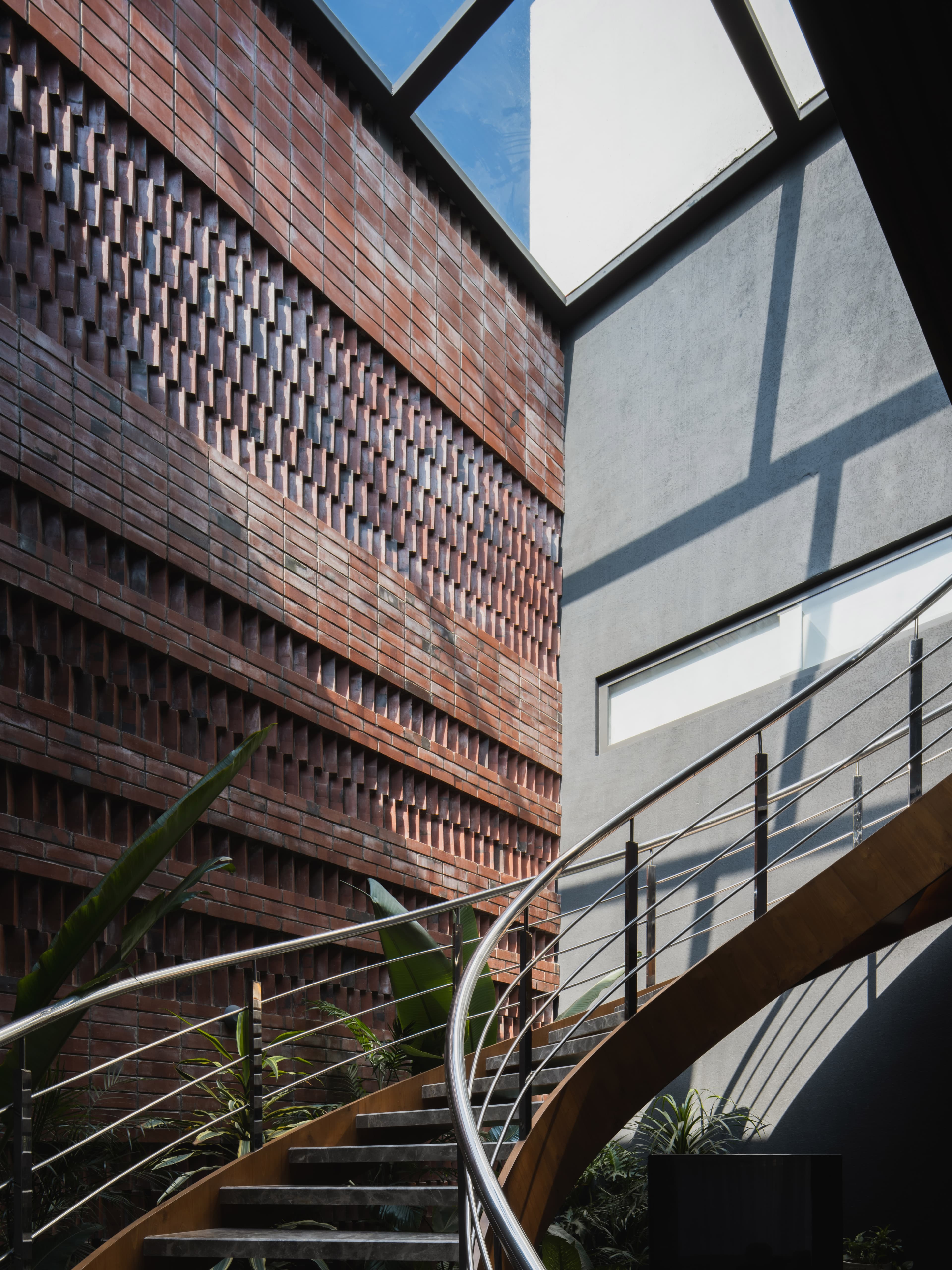 Exposed brick jaali, curved staircase, and skylight create a dramatic interplay of light, texture, and indoor-outdoor spatial fluidity.