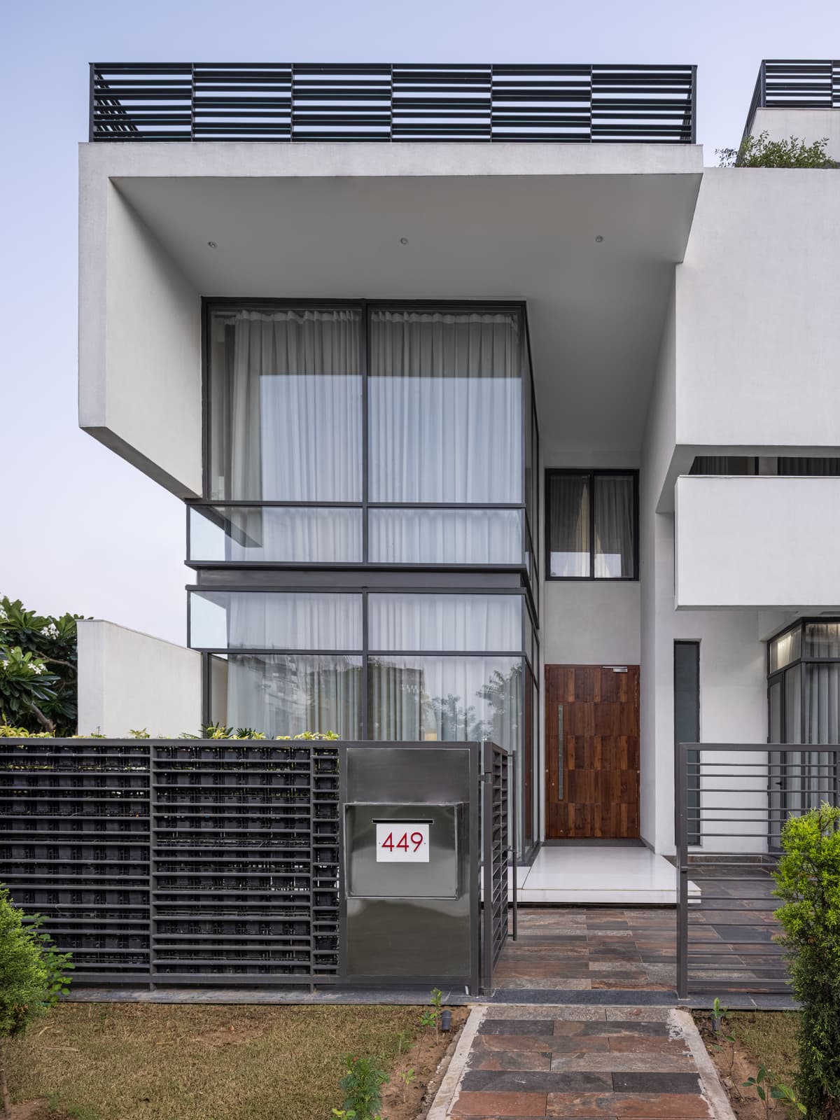 Minimalist entrance framed by a cantilevered volume; vertical glazing, warm wood door, and metal fencing emphasize clean, modern architectural language.