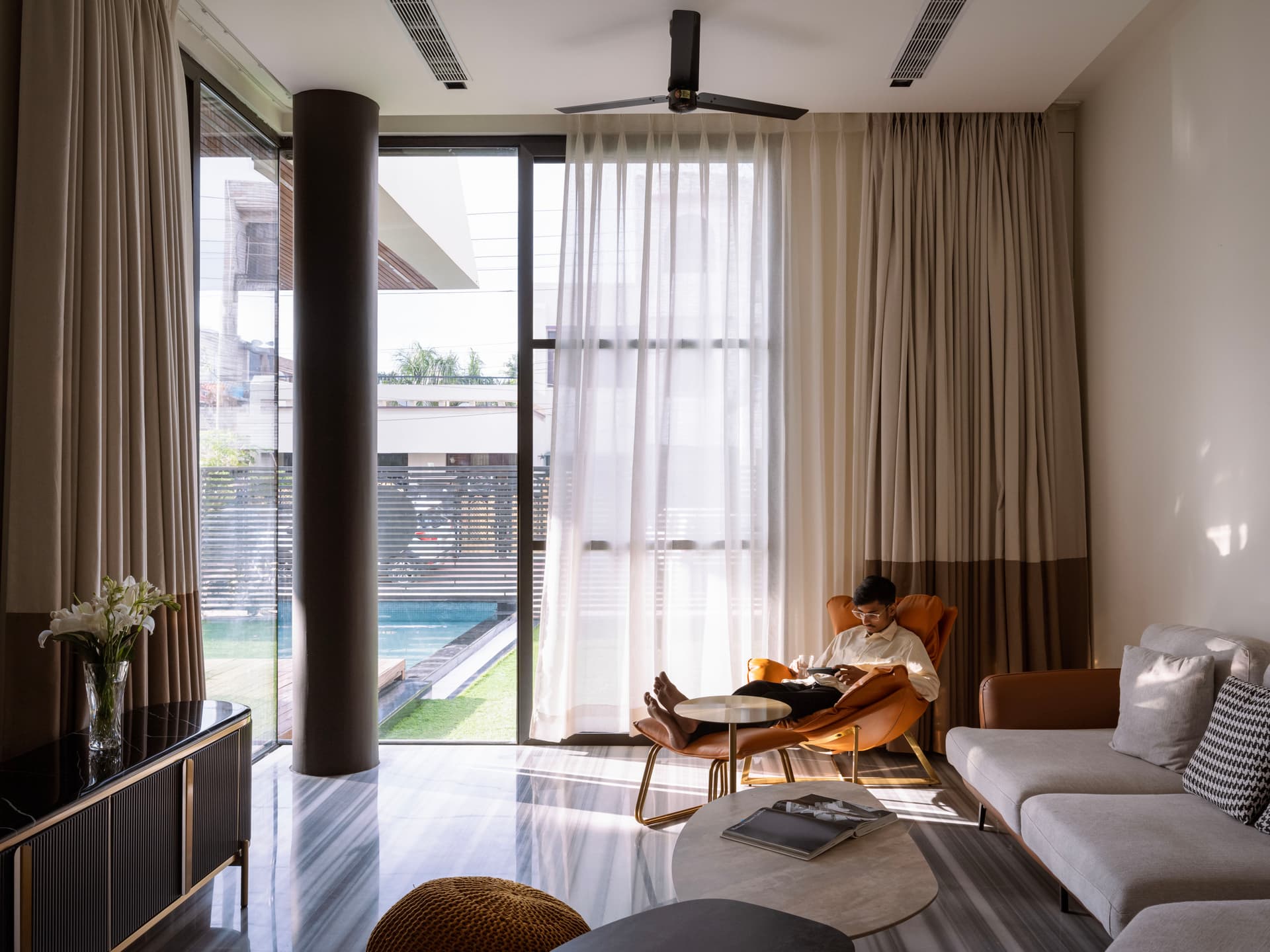 Floor-to-ceiling glazing, soft-toned drapery, and striped marble flooring infuse the lounge with natural light, elegance, and outdoor connectivity.