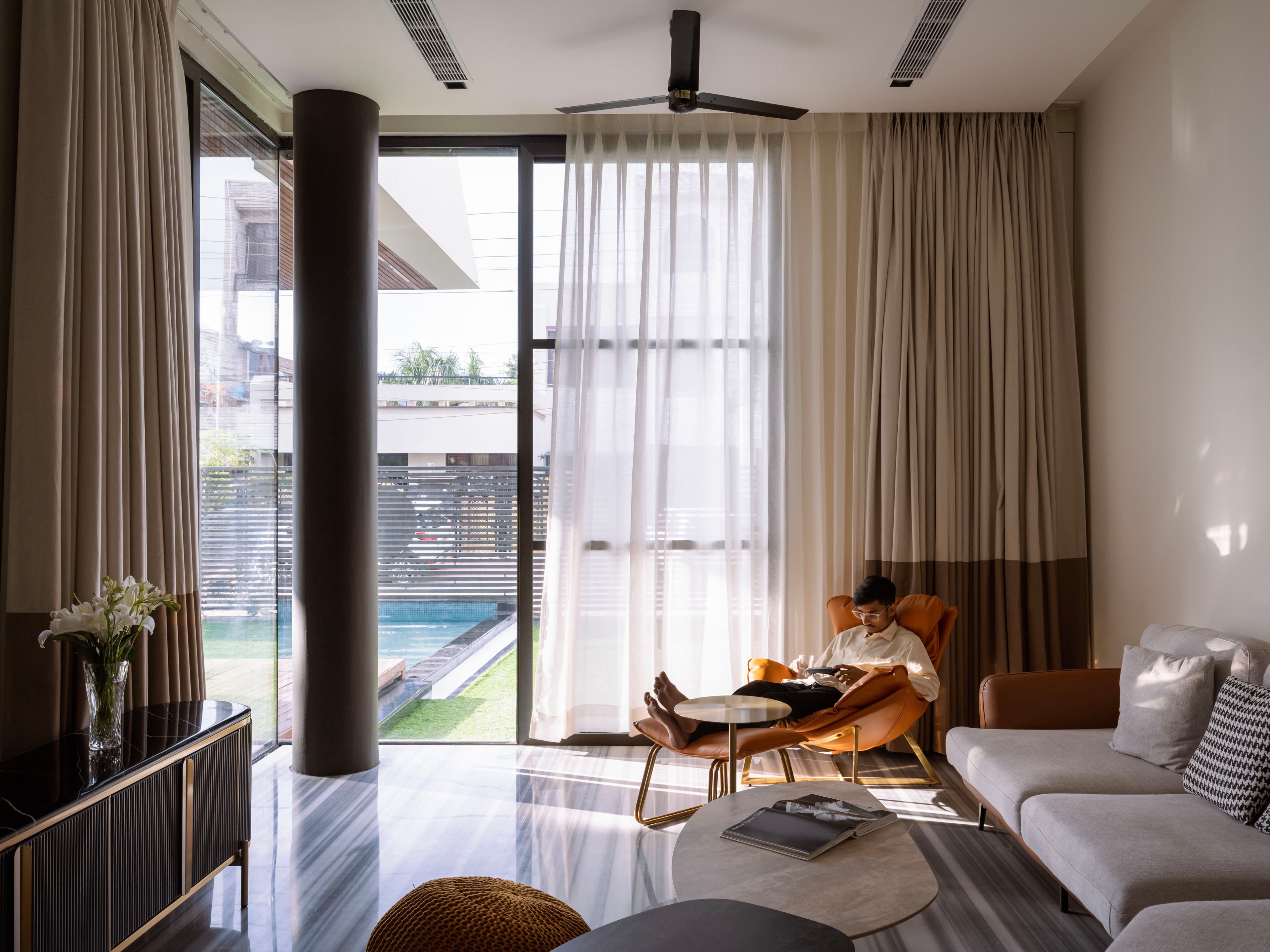 Floor-to-ceiling glazing, soft-toned drapery, and striped marble flooring infuse the lounge with natural light, elegance, and outdoor connectivity.